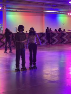 two people standing on skateboards in an indoor area with colorful lights and decorations behind them