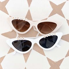 two pairs of white sunglasses with brown lenses on top of a patterned wallpaper background