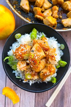 a black bowl filled with rice and chicken on top of a wooden table next to an orange