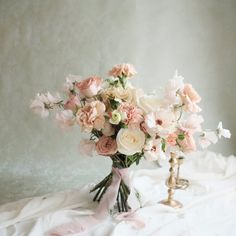 a bouquet of flowers sitting on top of a white cloth covered bed next to a golden candle