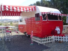 a red and white trailer parked next to a table with chairs on top of it