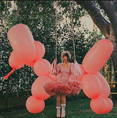 a woman sitting on a swing with pink balloons