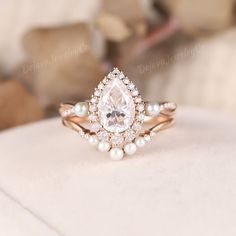 an engagement ring with a pear shaped diamond surrounded by white pearls on a cushioned surface