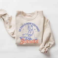 "So This Is How You Make Biscuits": This baking cat sweatshirt makes a totally unique gift for any baker or cat lover. Grab this sweater today while it's on sale! Delivery Times: ◦ Production: 1 business day (avg.)  ◦ Shipping: 3 business days (avg.) Overview: Ultra-Comfy Feel: The air-jet spun yarn creates a luxuriously soft feel against your skin, perfect for lounging or layering. Classic Fit: Perfect for that oversized look or just a classic fit. The relaxed silhouette with ribbed cuffs and w Raccoon Shirt, Raccoon Funny, Cat Sweatshirt, Funny Sweatshirts, Jesus Shirts, Funny Graphics, Clothes Horse, Vintage Sweatshirt, Air Jet