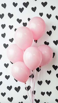 a bunch of pink balloons sitting on top of a white and black wall with hearts drawn on it