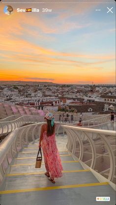 a woman in a pink dress is walking up some stairs and looking at the sunset