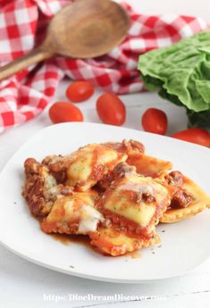 a white plate topped with lasagna covered in sauce and cheese next to lettuce