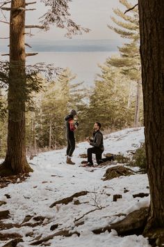 two people sitting in the snow near some trees