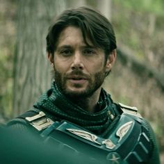 a man dressed in armor standing next to a tree and looking off into the distance