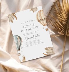 a wedding card with hot air balloons and palm leaves on the bed next to it