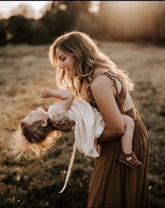 a woman holding a baby in her arms while standing on top of a grass covered field