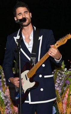 a man in a suit singing into a microphone and playing an electric guitar on stage