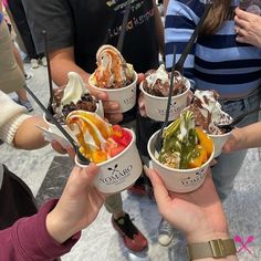 several people holding up ice cream bowls with toppings