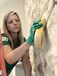 a woman in green gloves cleaning a brick wall with a sponge and a paint roller