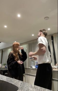 two people standing in a kitchen talking to each other