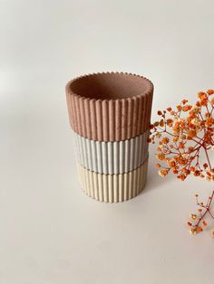 a vase with some flowers next to it on a white surface and one is made out of clay