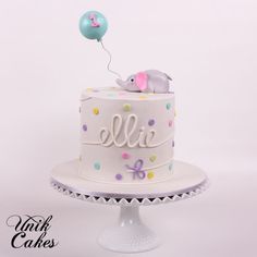 a white cake with an elephant on top and balloons in the air above it that says lilie