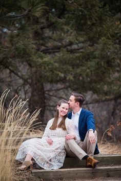 a man and woman sitting on steps in front of some tall grass with trees behind them