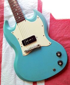 a blue electric guitar sitting on top of a red and white striped sheet with black knobs