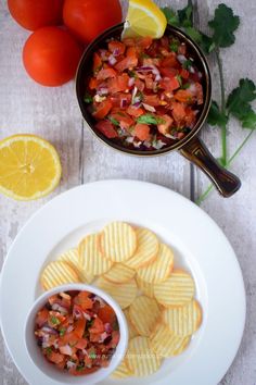 a white plate topped with potato chips next to a bowl of salsa and lemon wedges