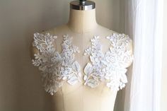 a mannequin with white lace and flowers on it's back, sitting in front of a window