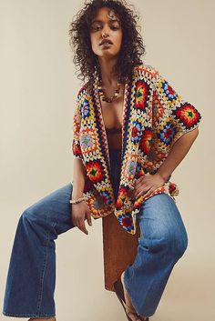 a woman sitting on top of a wooden bench wearing jeans and a crocheted jacket