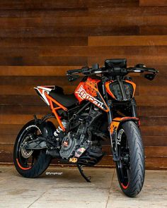 an orange and black motorcycle parked in front of a wooden wall