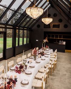 a long table set up with candles and place settings in front of large glass windows