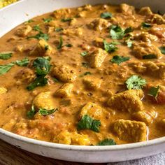 a white bowl filled with meat and veggies covered in sauce, garnished with cilantro