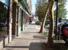 the sidewalk is lined with parked cars on both sides and trees in front of them