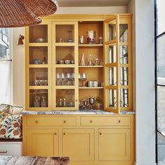 a yellow china cabinet with glass doors in a living room next to a large window