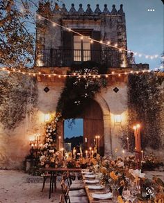 an outdoor dining area with lights strung over the table and chairs, surrounded by greenery