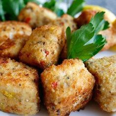 some fried food on a white plate with lemon wedges and parsley garnish