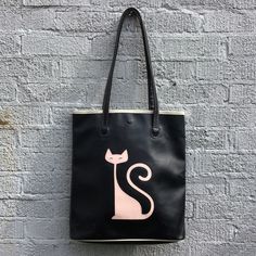 Vintage RedTango by TokyoBay black vinyl tote bag with white vinyl trim, and pink Mid-century modern atomic cat appliqué, c. 2000. The bag measures 15 x 14 x 2 3/4" with 12" shoulder straps. It is in very good condition with a few light exterior surface scuff marks. Both straps are undamaged and show no signs of wear and the interior lining of the tote is undamaged. The stitching is also complete and fully intact; the black snap closure is a replacement. Please see photos for details. Black Reversible Shopping Bag, Black Travel Bag With Cat Design, Reversible Black Shopping Bag, Reversible Black Bags For Shopping, Black Rectangular Bag With Cat Print, Black Rectangular Bag With Cat Design, Black Cat Print Rectangular Shoulder Bag, Black Rectangular Shoulder Bag With Cat Print, Rectangular Black Shoulder Bag With Cat Print