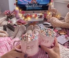 two pink mugs filled with candy sitting in front of a tv