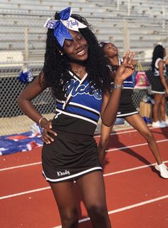 a cheerleader standing on a track with her hands in the air and smiling at the camera