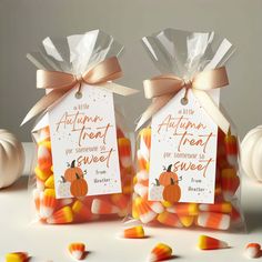 two bags filled with candy corn sitting on top of a white table next to pumpkins