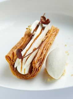 a white plate topped with a pastry covered in icing next to a scoop of ice cream