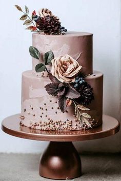 a three tiered cake with flowers and leaves on top is sitting on a table