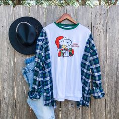 a white shirt with a snoopy christmas design on it next to jeans and a cowboy hat