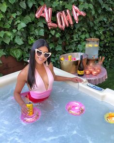 a woman in a pink bathing suit and sunglasses sitting in a hot tub with drinks