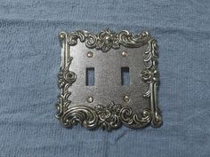 an ornate metal switch plate cover on a blue cloth with the light switch in the middle