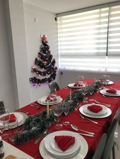 the table is set for christmas dinner with red napkins and white plates, silverware