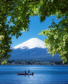 two people on a boat in the water with a mountain in the background