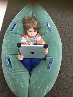 a little boy sitting in an inflatable boat using a laptop