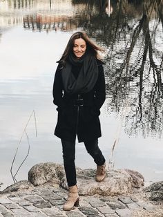 a woman standing on top of a rock near water