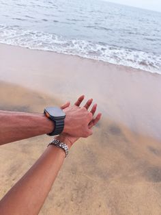 two people holding hands on the beach with waves in the water and sand behind them