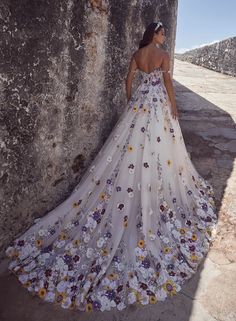 a woman standing next to a stone wall wearing a white dress with flowers on it