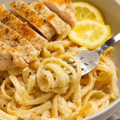 a white bowl filled with pasta and chicken next to lemon wedges on a table