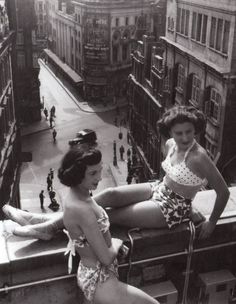 two women in bathing suits sit on the roof of a building and look off into the distance